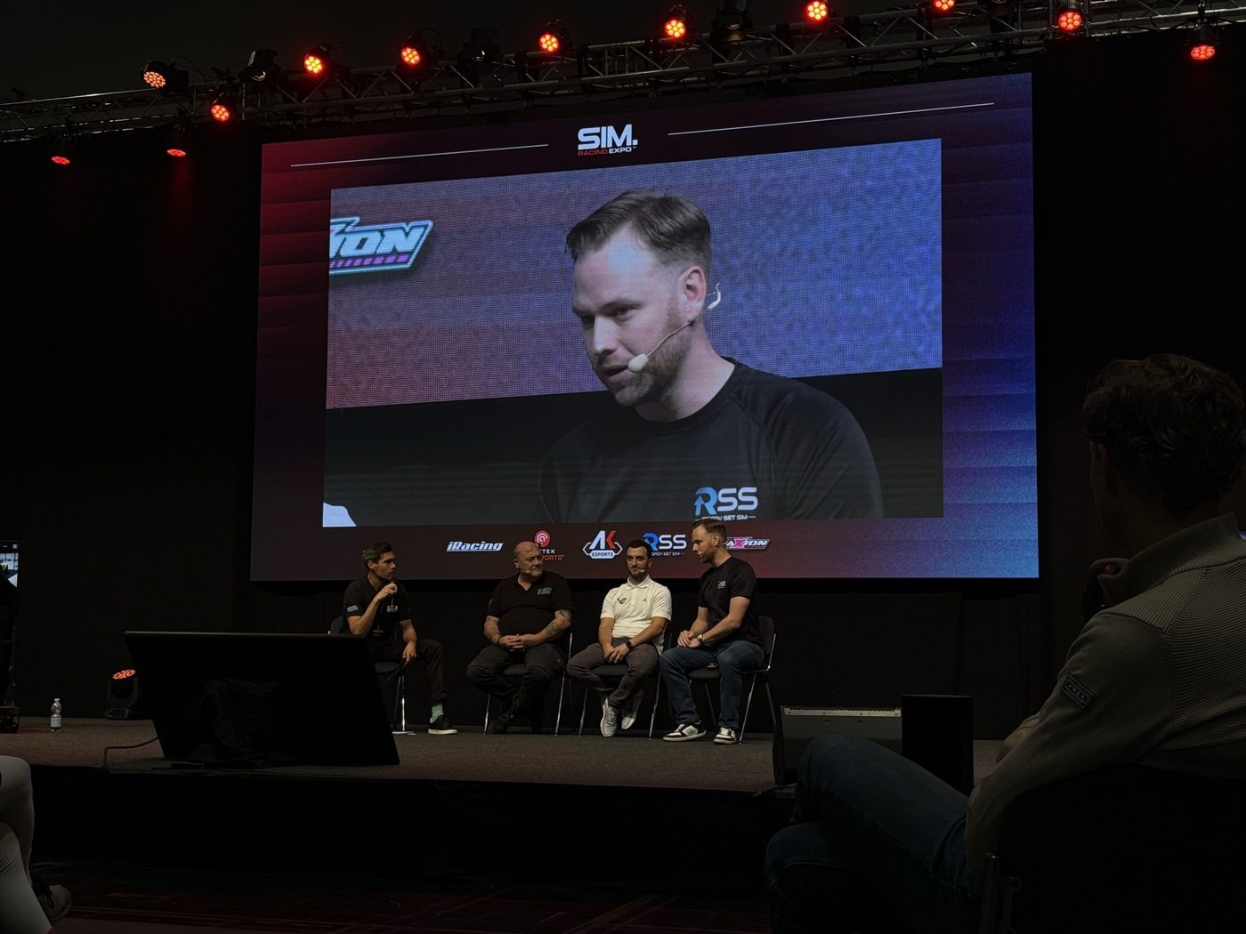 Ian Strohmen on the big screen during a Sim Racing Expo panel, wearing a Ready Set Sim shirt